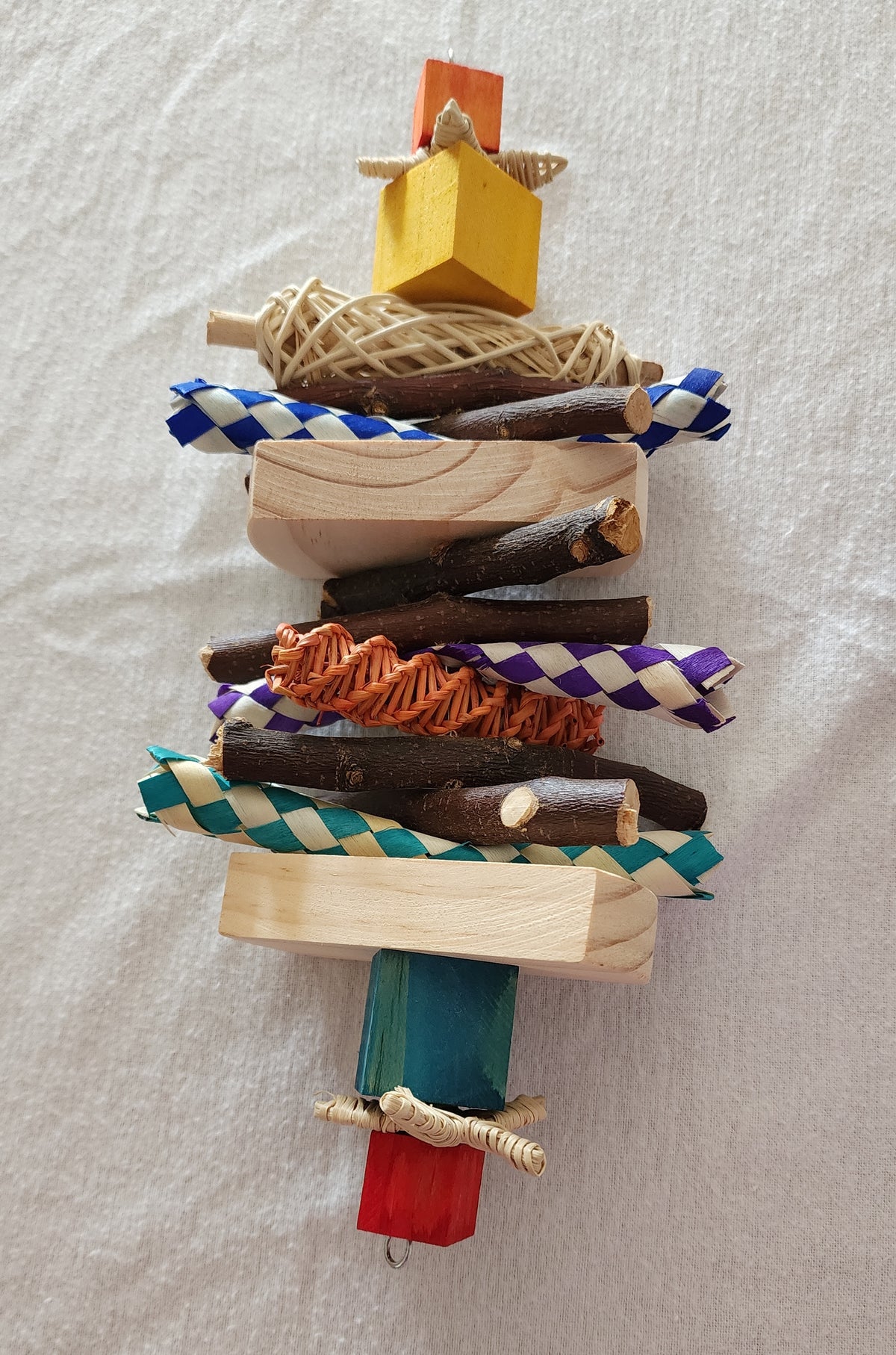 A colorful pet chew toy made of pine wood and bamboo shredders, decorated with a small apple stick and a loofah slice.
